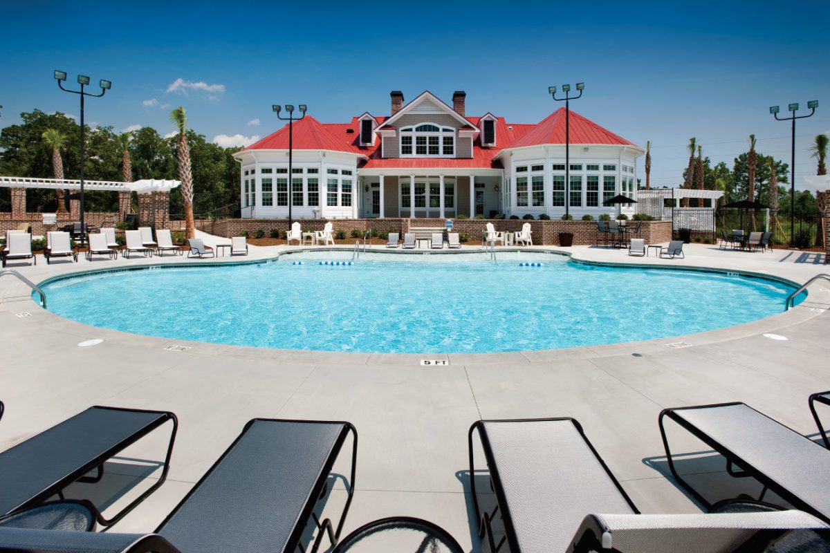 Sparkling, resort-style pool at daytime with ample poolside lounge chairs in front of the white clubhouse with a red roof