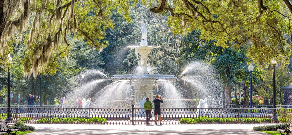 Two people walking in front of a large fountain at Forsyth Park in Savannah Georgia